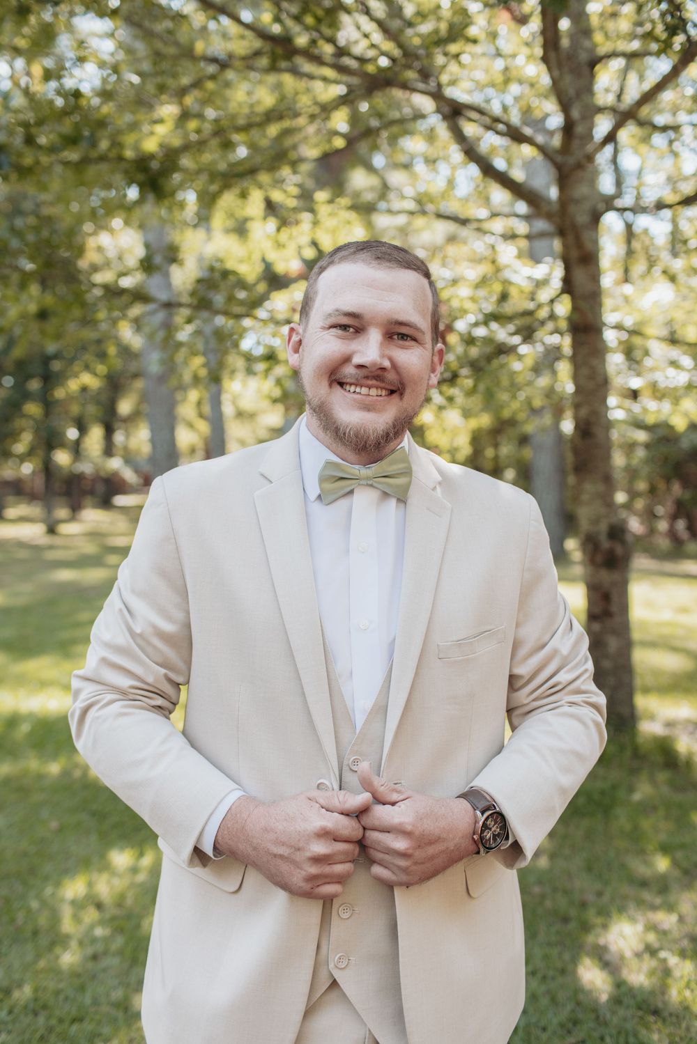 Groom in cream colored suit with mint green bowtie poses outdoors.