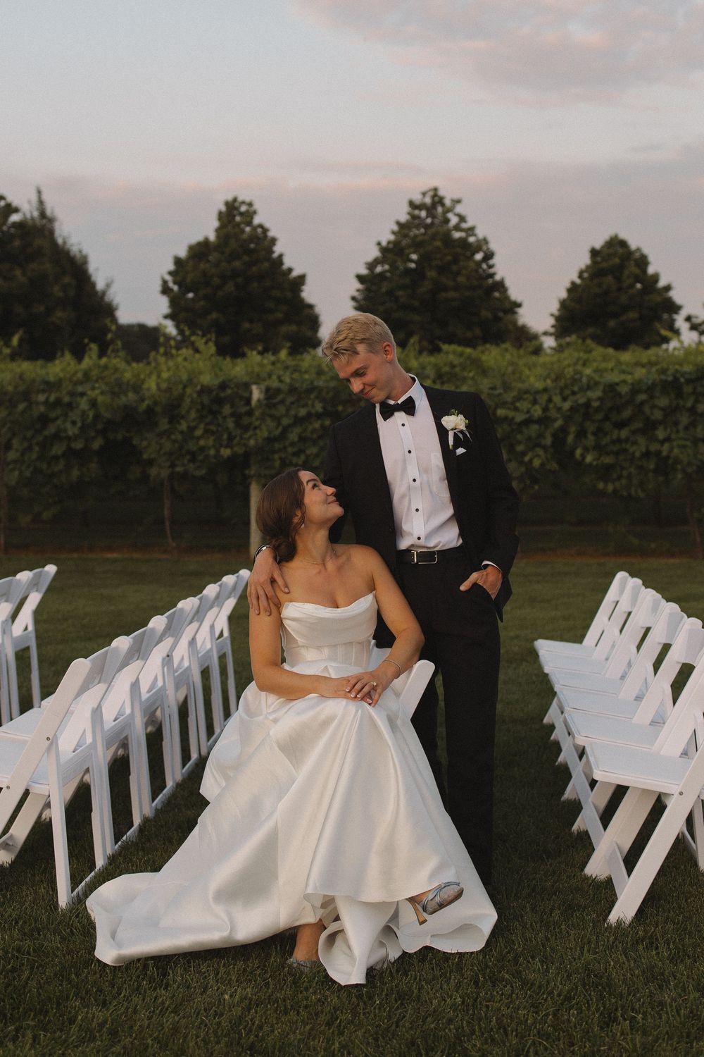 Newlyweds sharing a tender moment among rows of white wedding chairs at sunset.