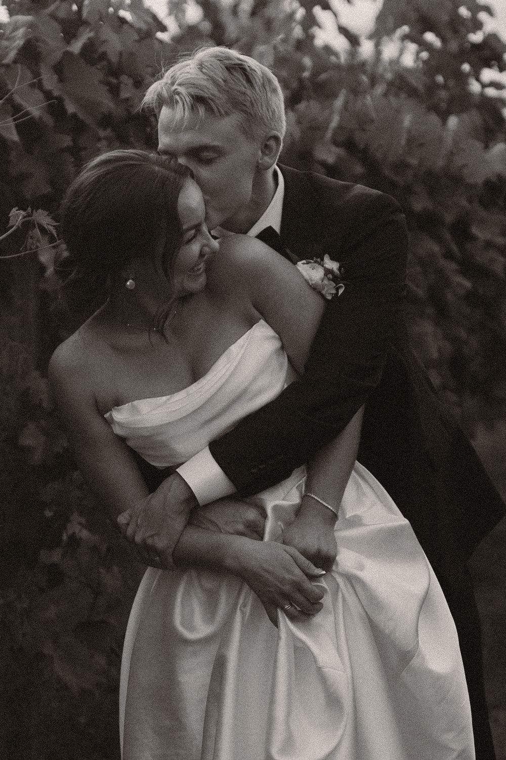 Black and white portrait of a couple's intimate embrace in a vineyard setting.