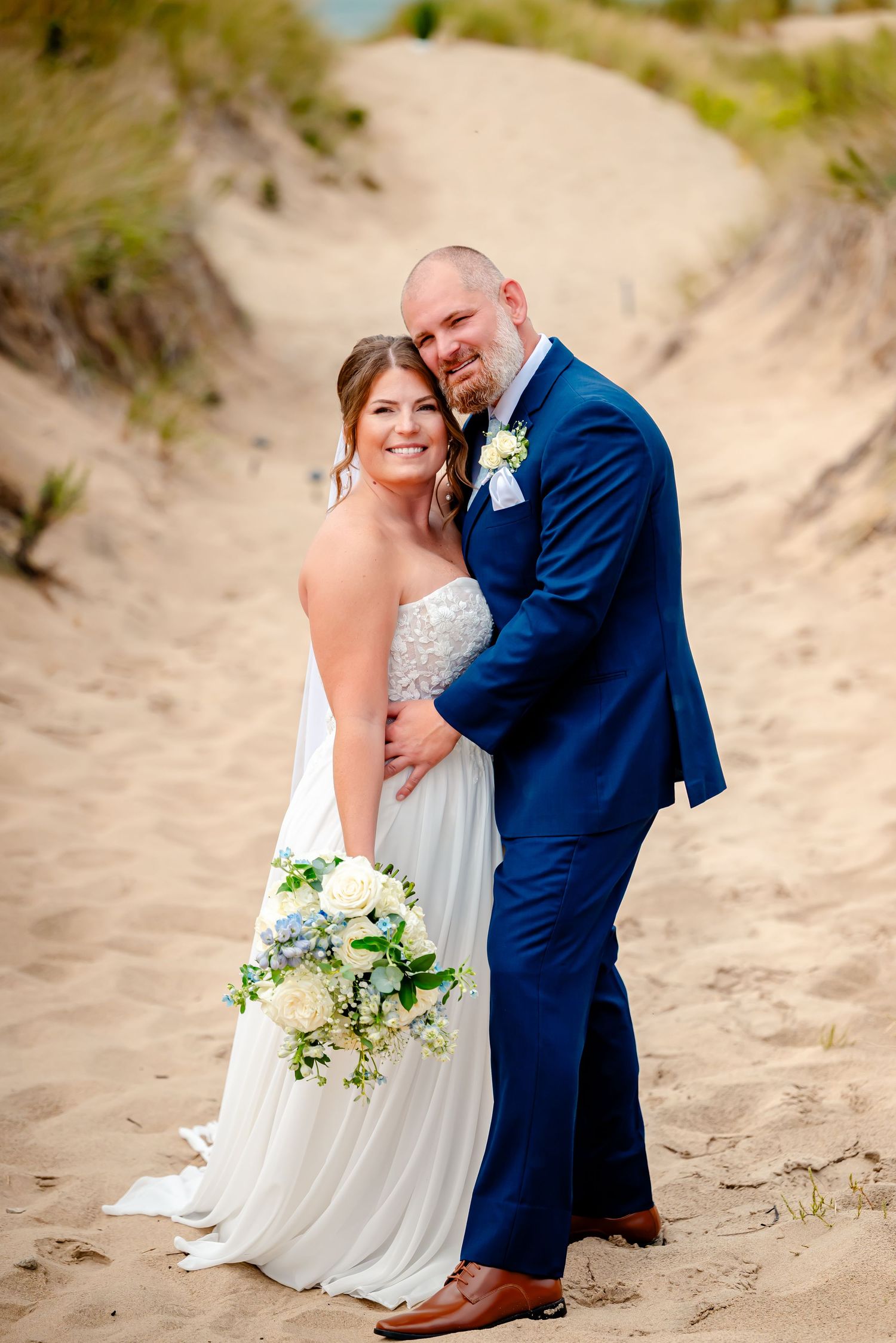 A couple shares romantic moments on sandy dunes during a beach wedding photoshoot.