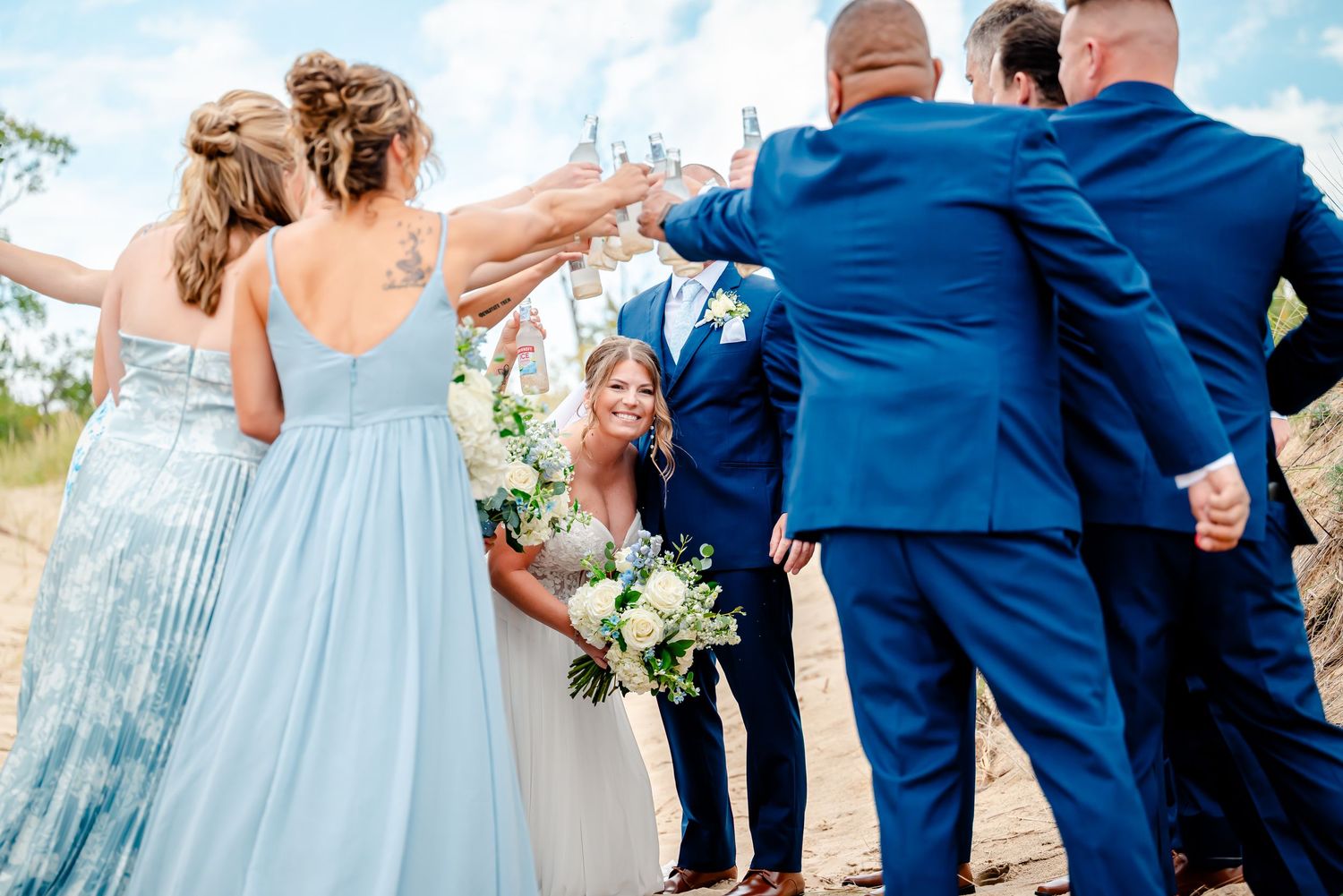 Wedding party members in navy blue and light blue attire dance together at an outdoor celebration.