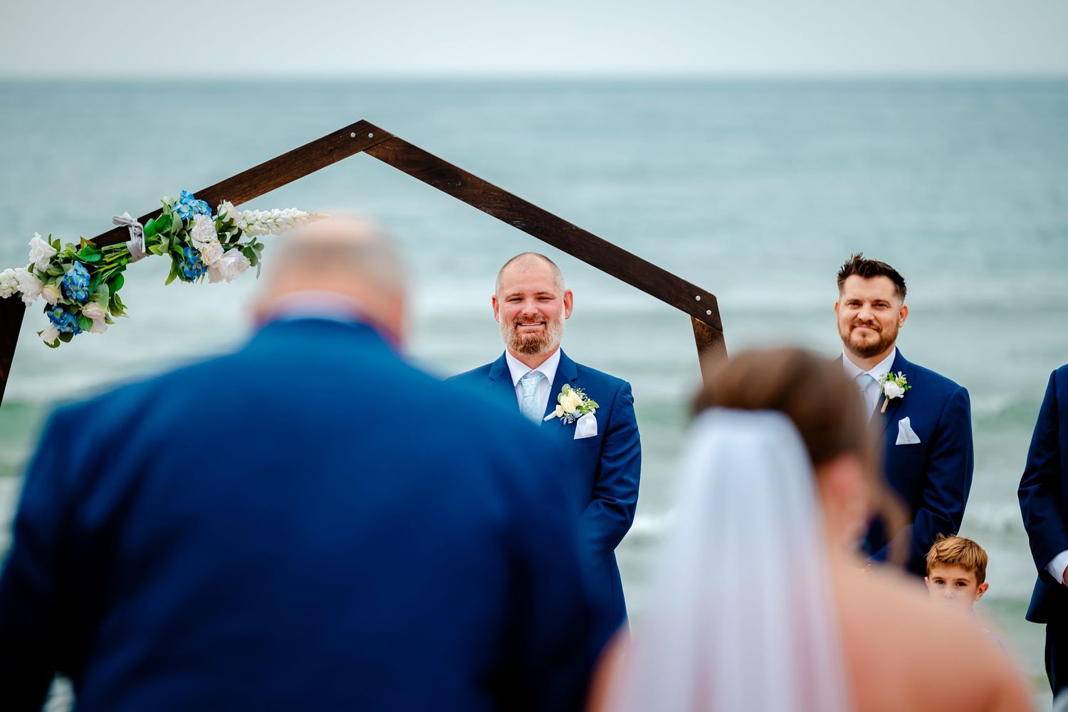 Emotional wedding ceremony moment captured during outdoor beach vows with blue ocean backdrop.