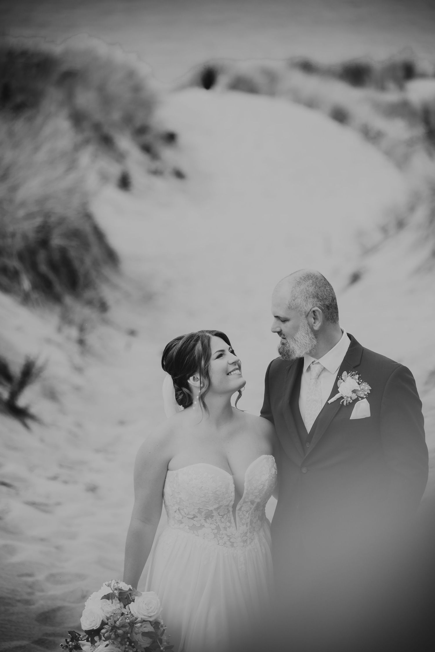 Black and white beach wedding photos showing intimate moments between a couple in romantic poses against sand dunes.