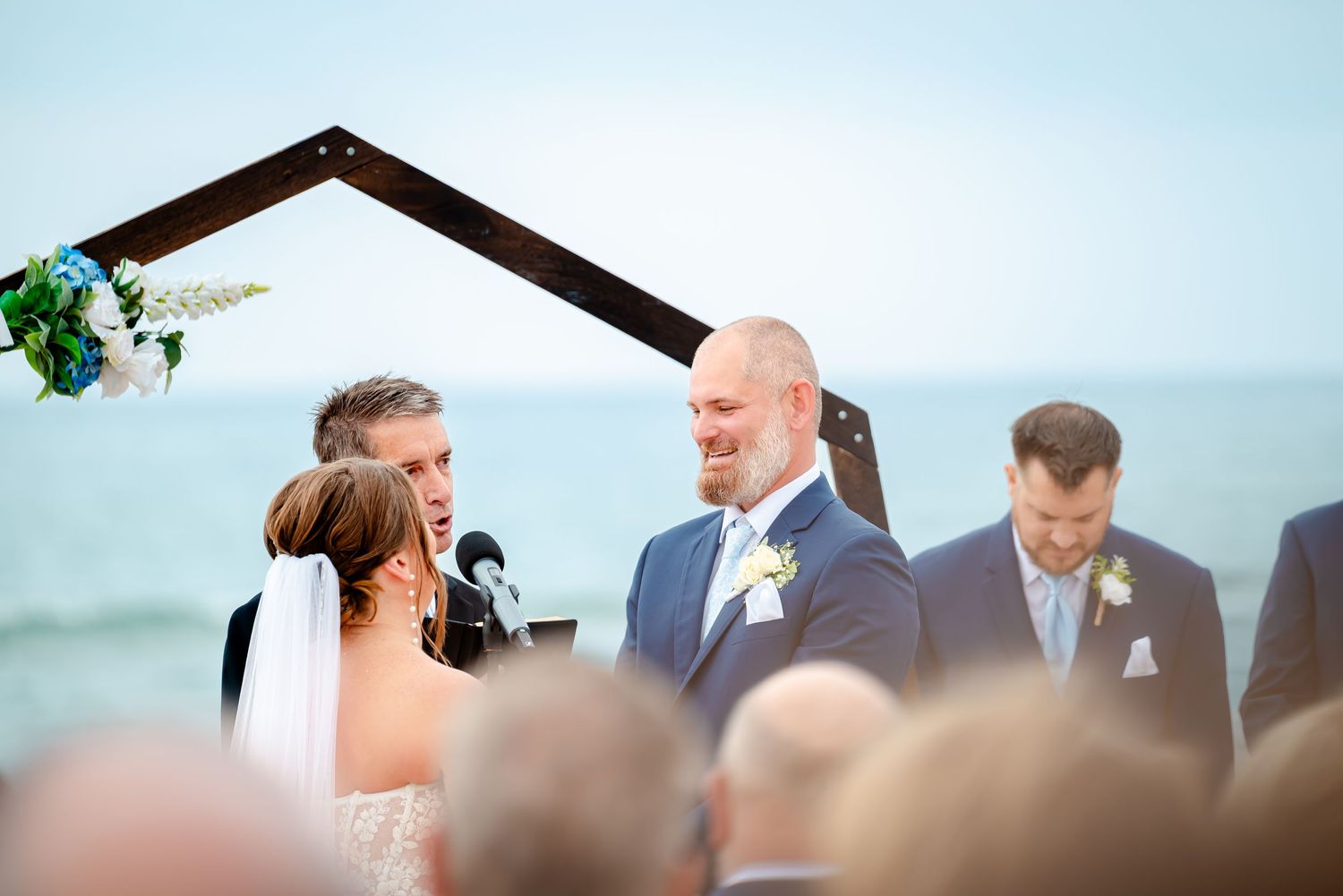 Scenic beachside wedding ceremony with wooden arch and greenery decorations against ocean view.