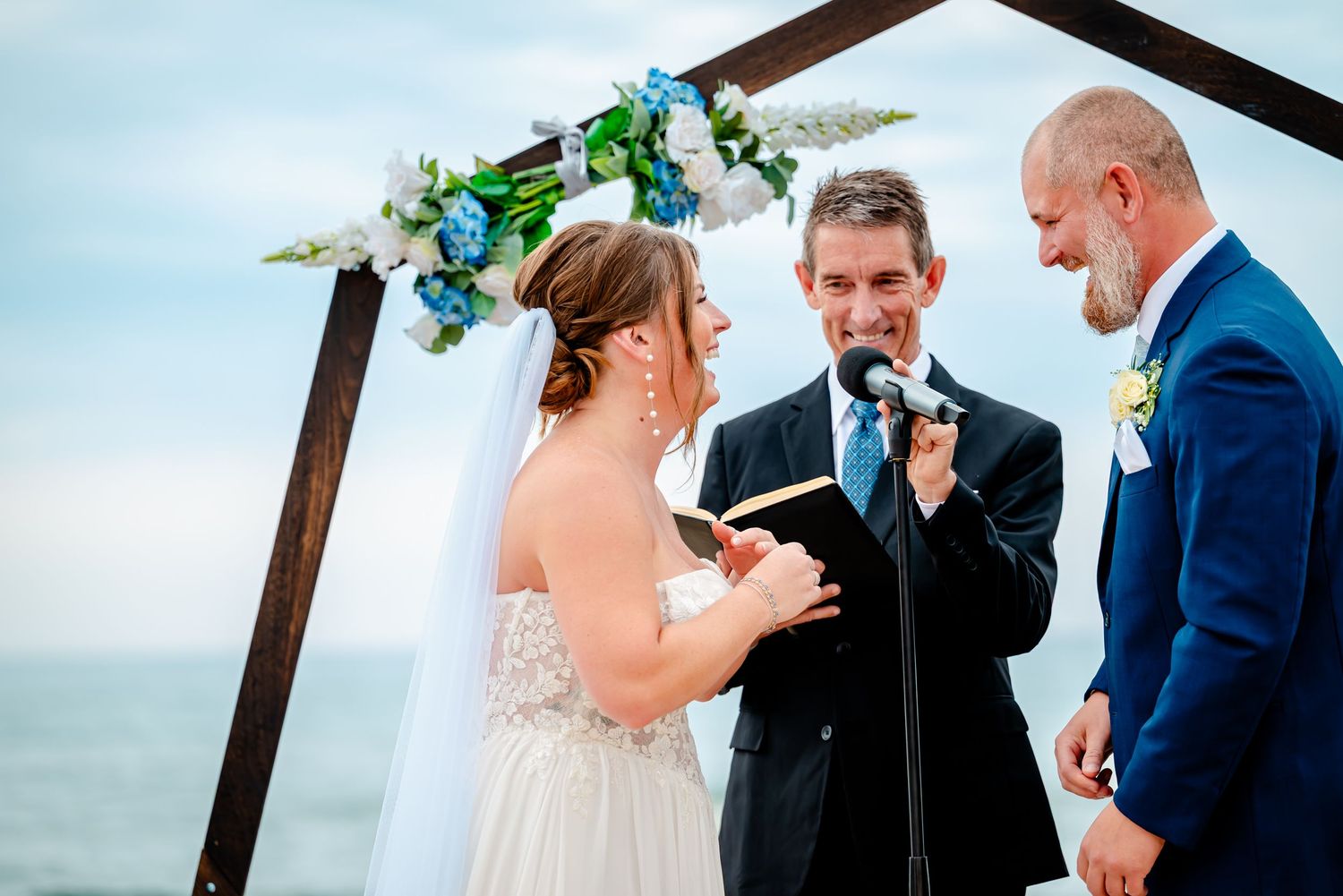 Outdoor beach ceremony under wooden arch with couple exchanging vows.