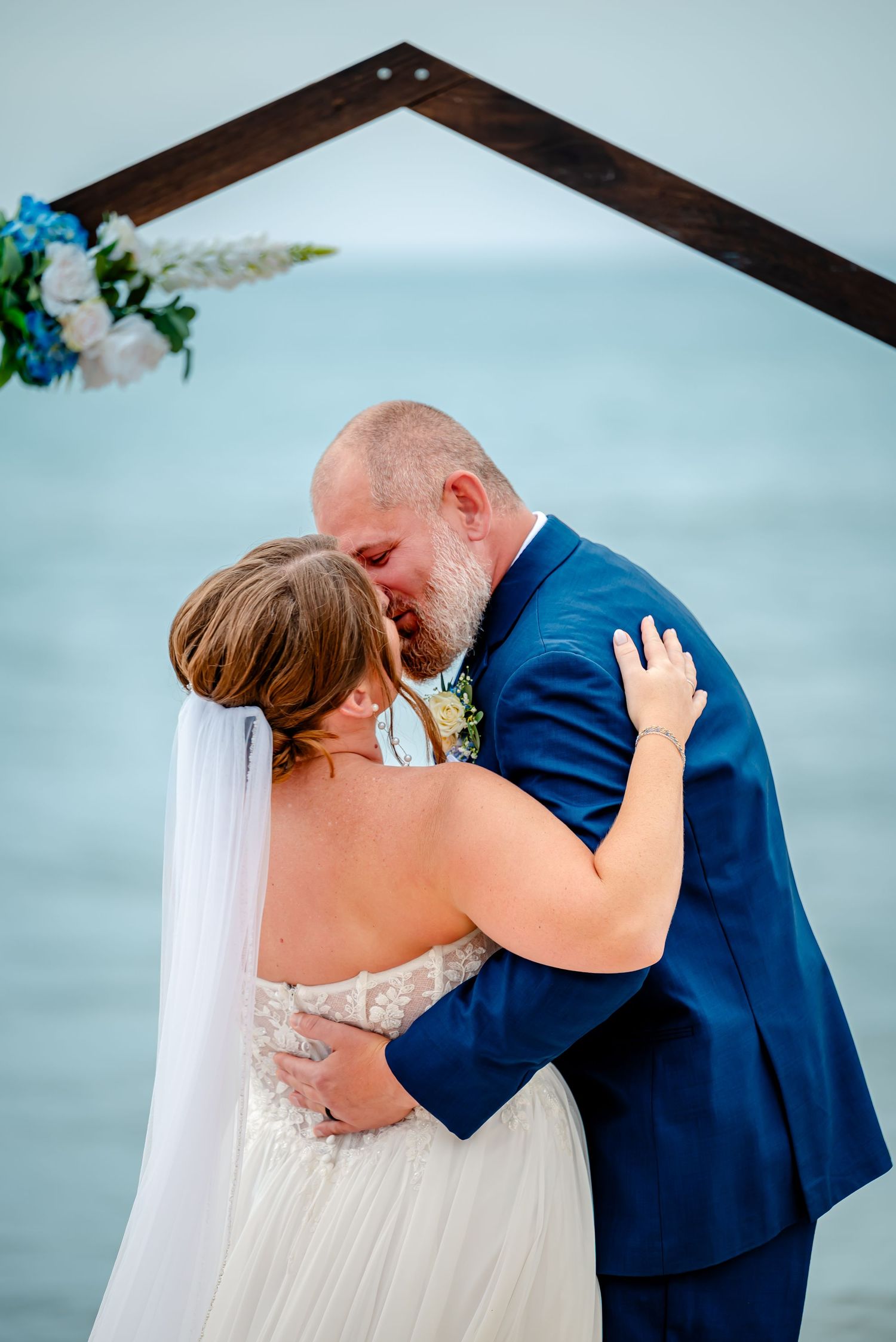 Intimate wedding couple embraces against a soft blue background.