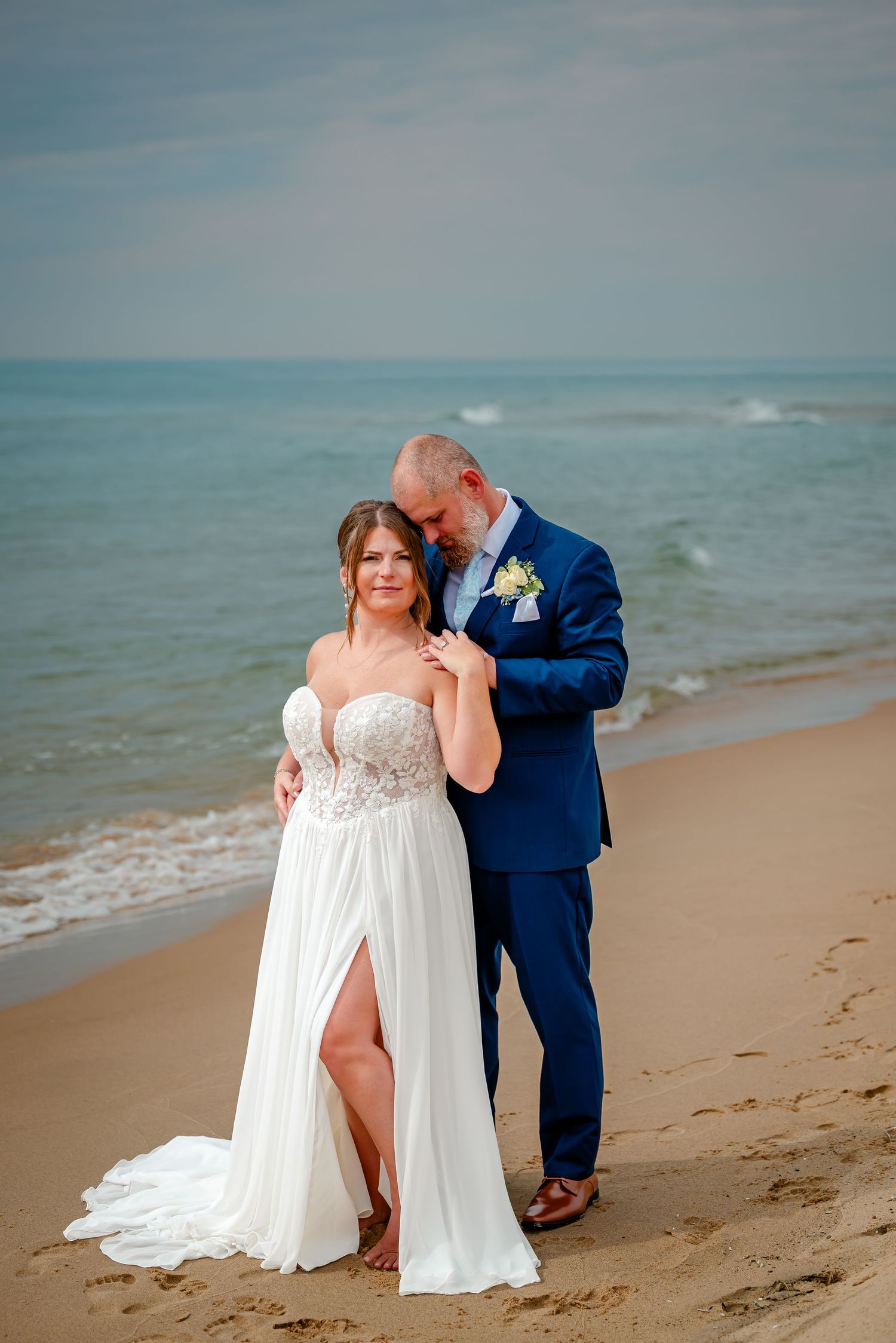 Newlyweds share intimate moments on a sandy beach with waves and ocean in the background.