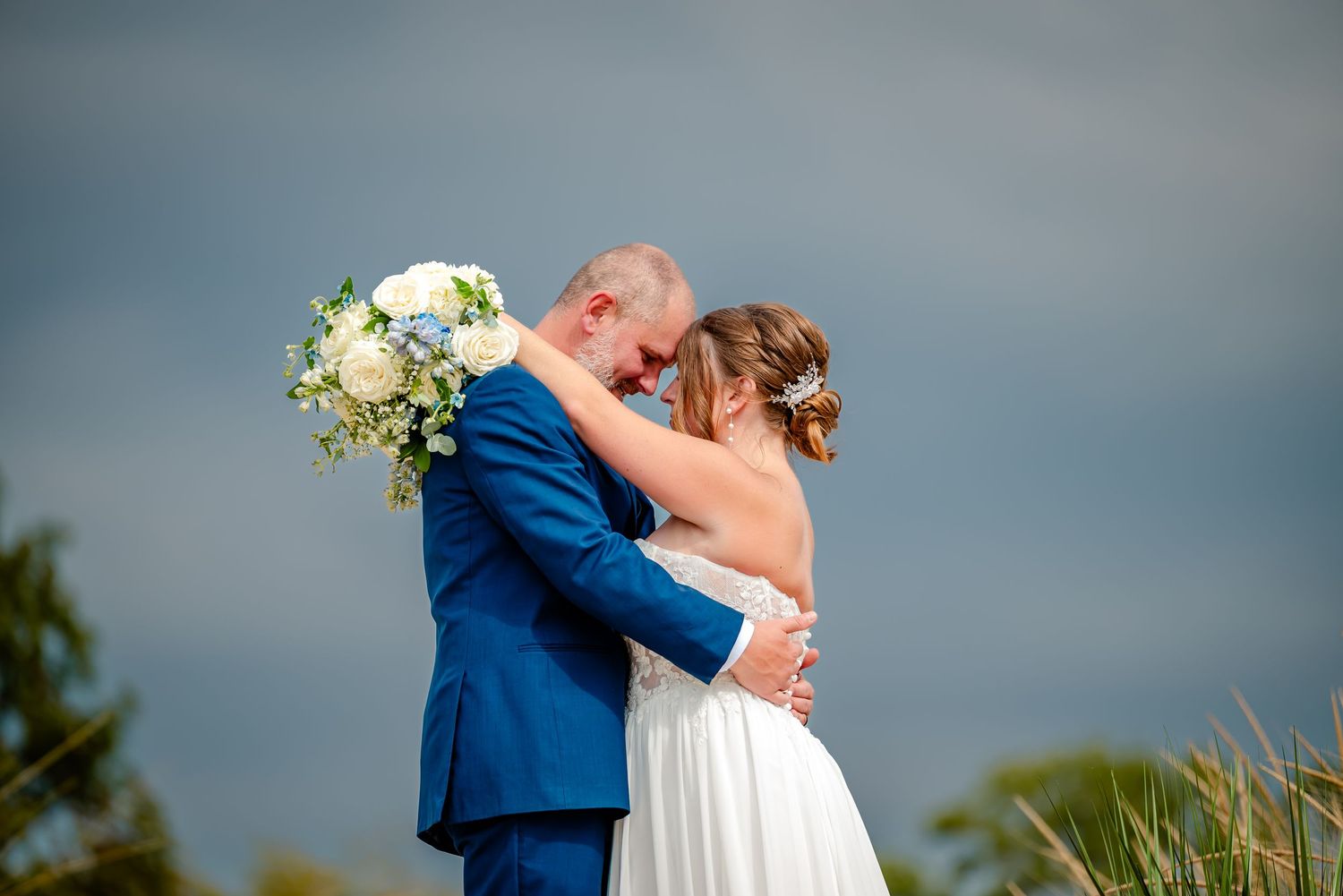 Newlyweds embrace against stormy sky backdrop during coastal wedding ceremony.