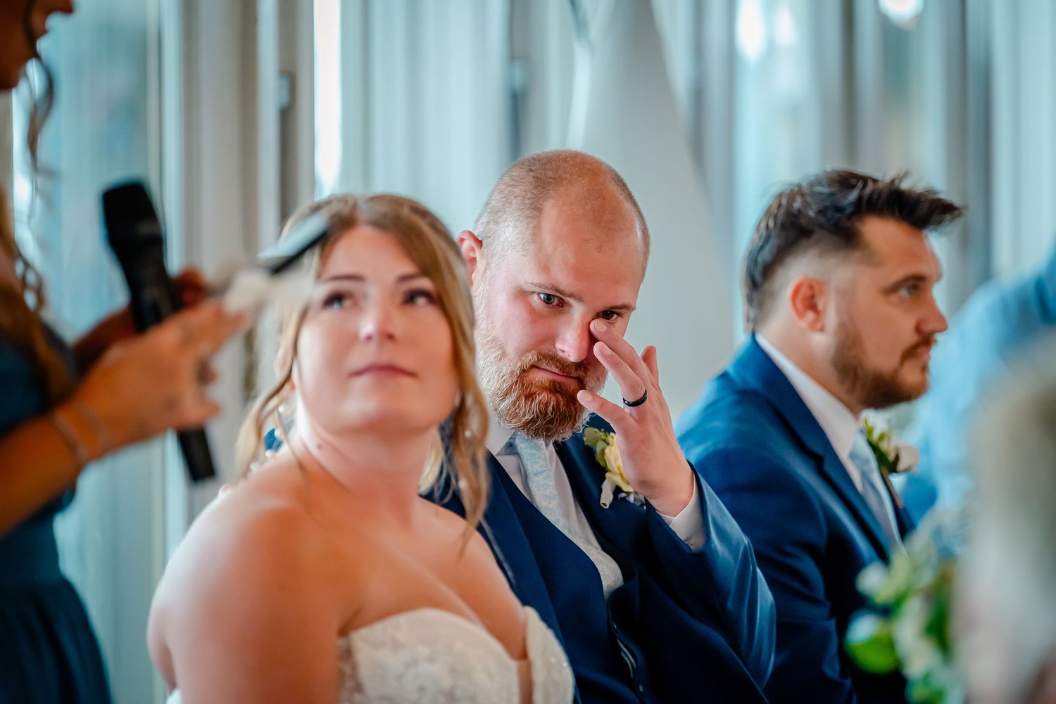 Wedding guests laugh and smile during an emotional reception speech in a bright banquet hall.