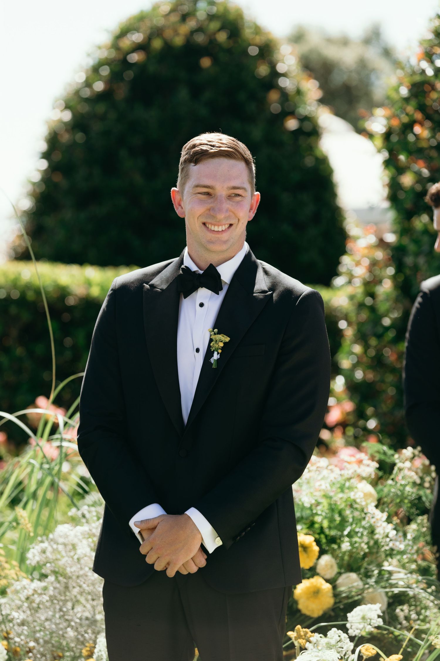 Three photos of someone in a black tuxedo posing in a sunny garden with yellow flowers and greenery in the background.