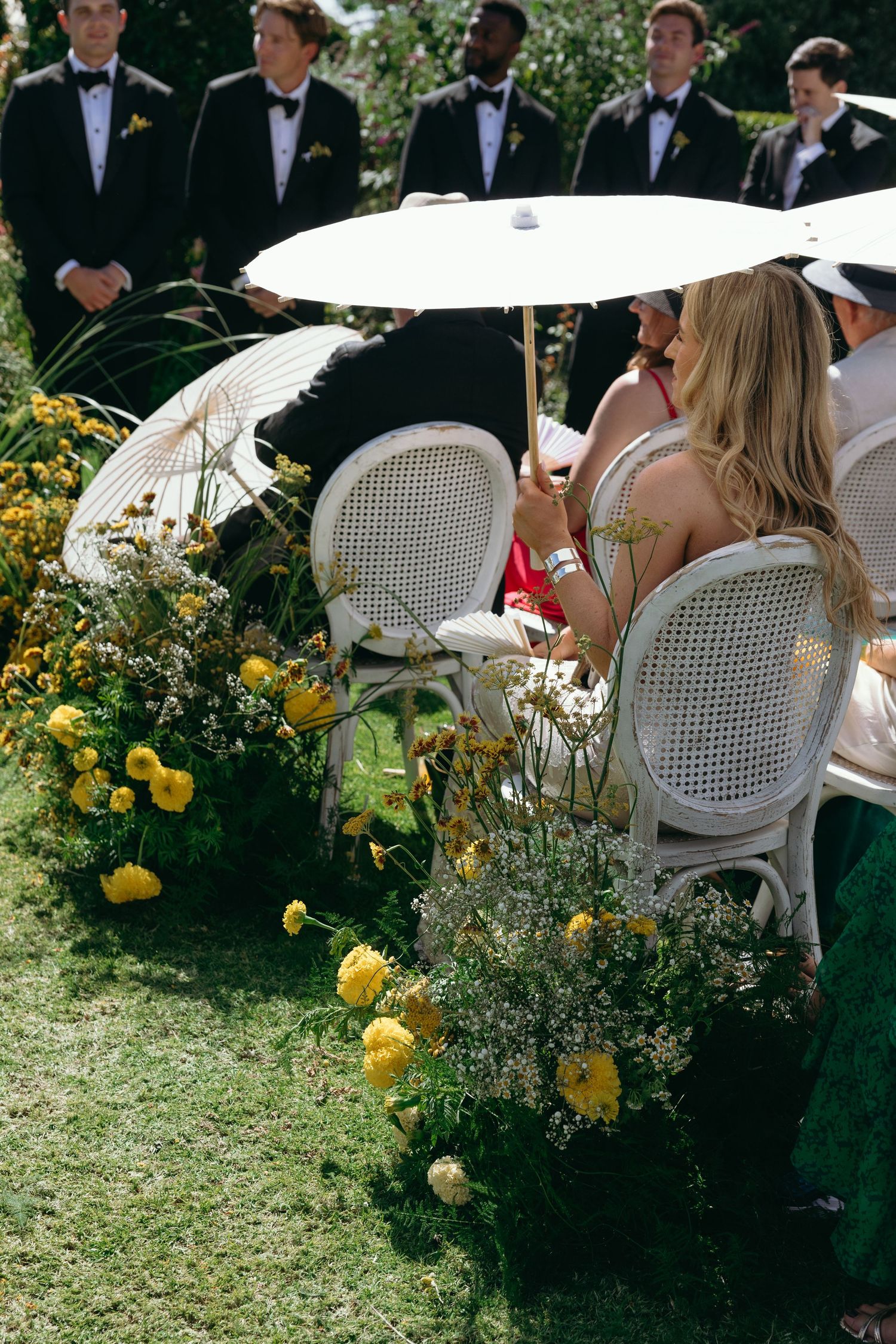 Elegant outdoor garden party setting with white parasols, wicker chairs and blooming yellow flowers.