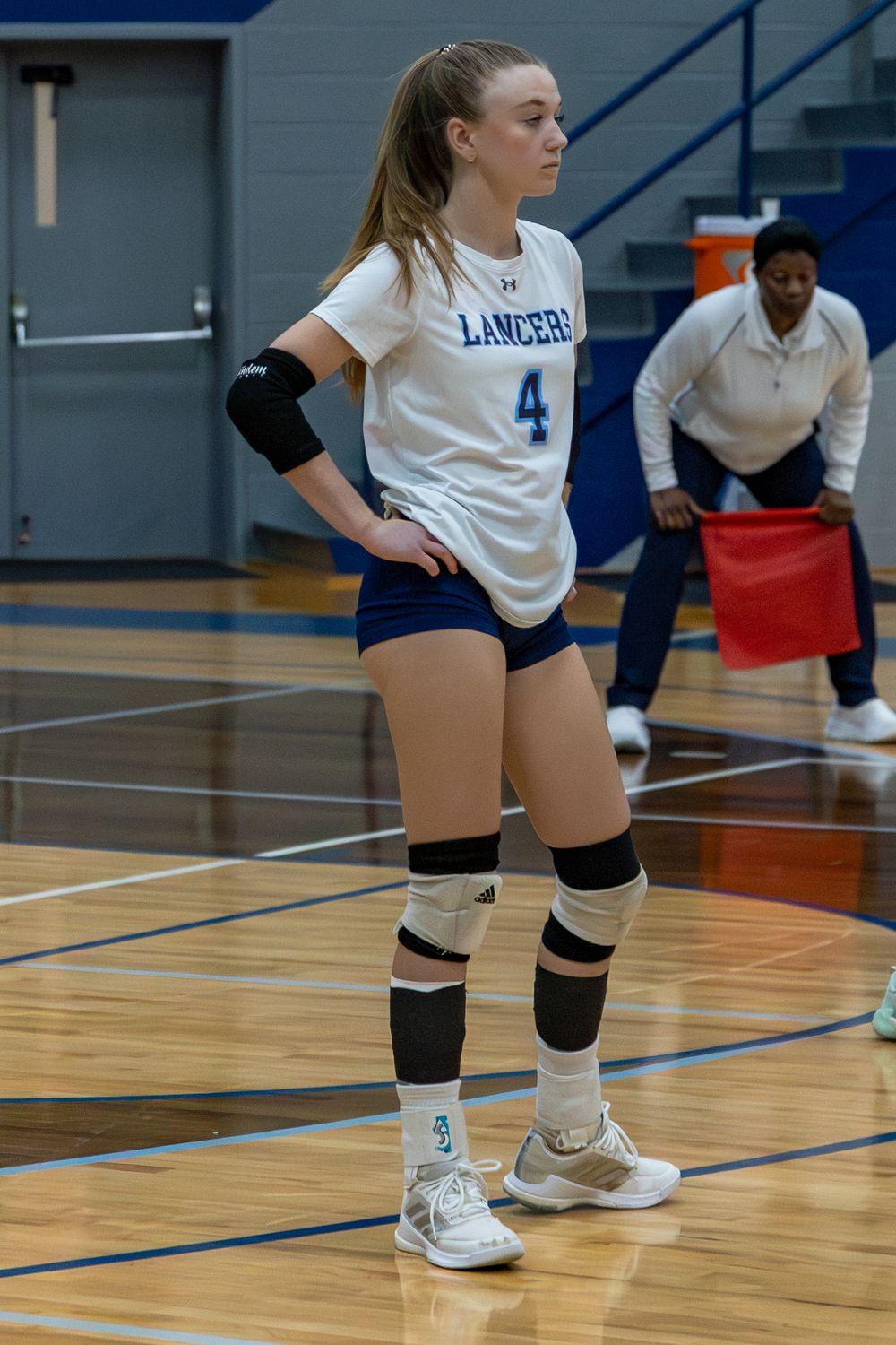 Volleyball players' legs and feet shown in defensive ready positions on a wooden gymnasium court during a match.