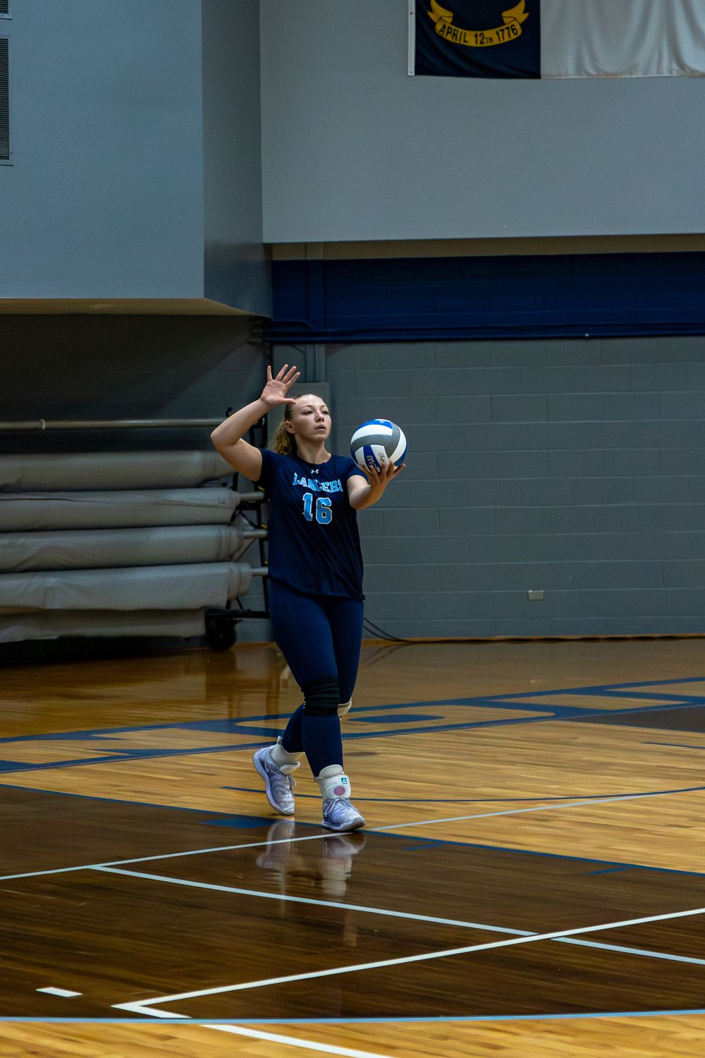Volleyball player in navy uniform diving low to save a ball during indoor practice.