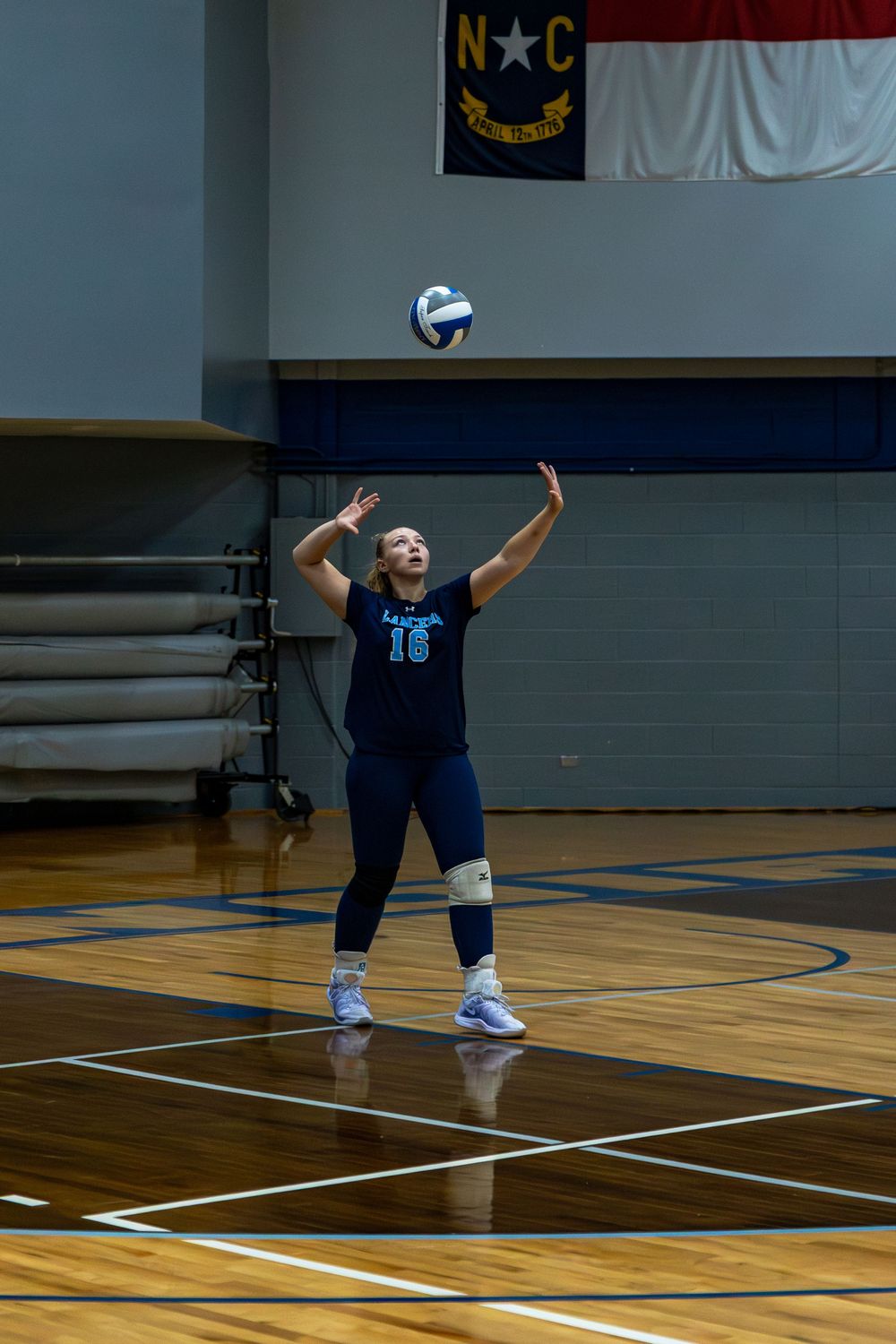 A volleyball player in a navy uniform performs a diving save on a gymnasium court during a match.