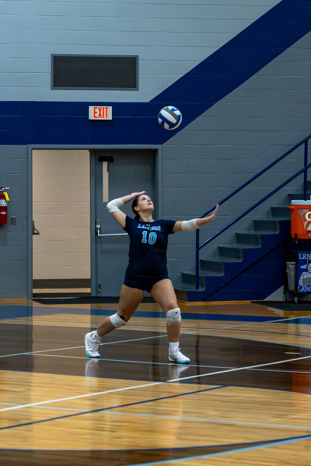 A volleyball player dives across the gym floor to save a ball during an indoor match.
