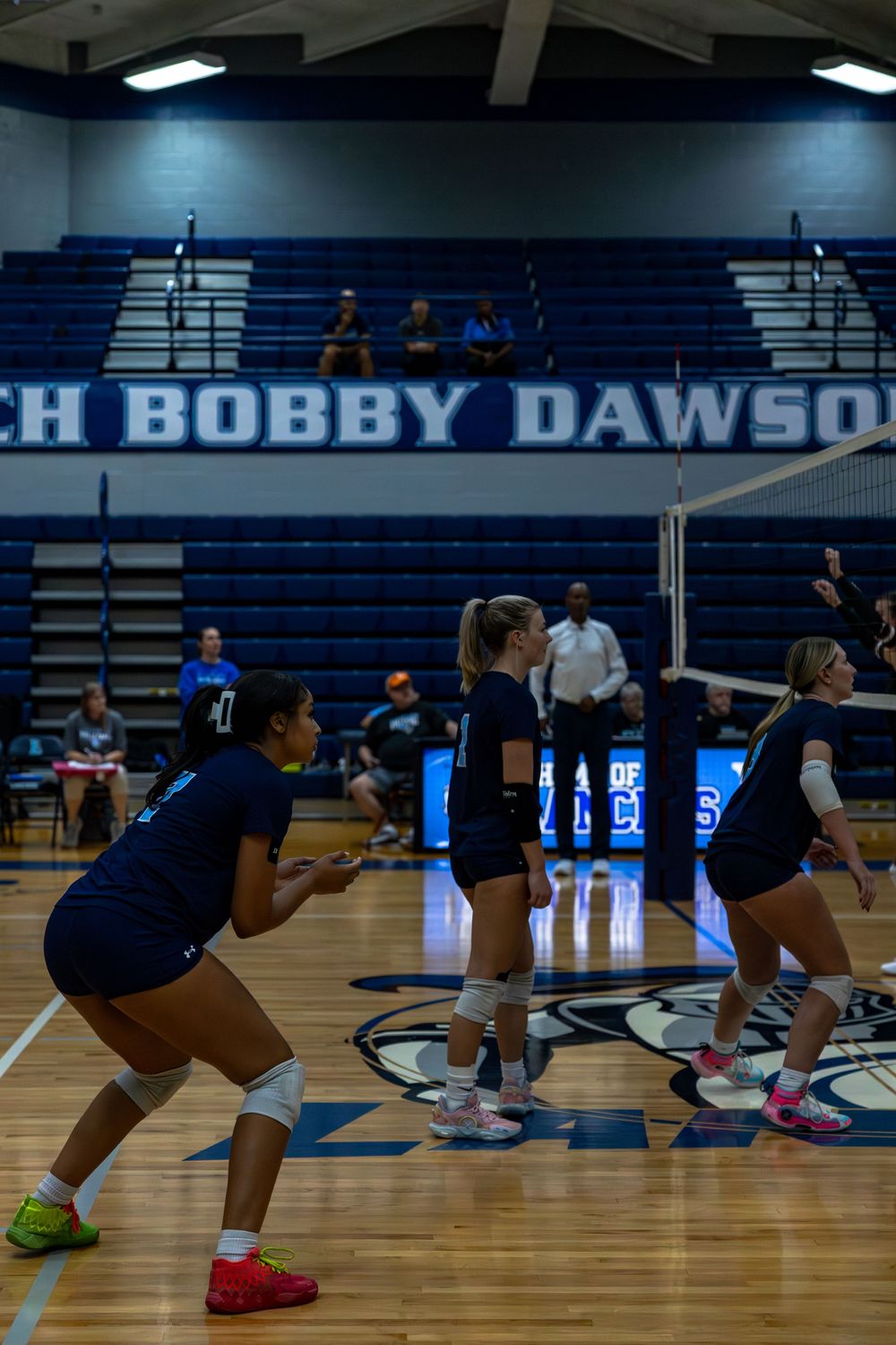 Female volleyball players perform synchronized defensive stance drills during practice in a gymnasium.