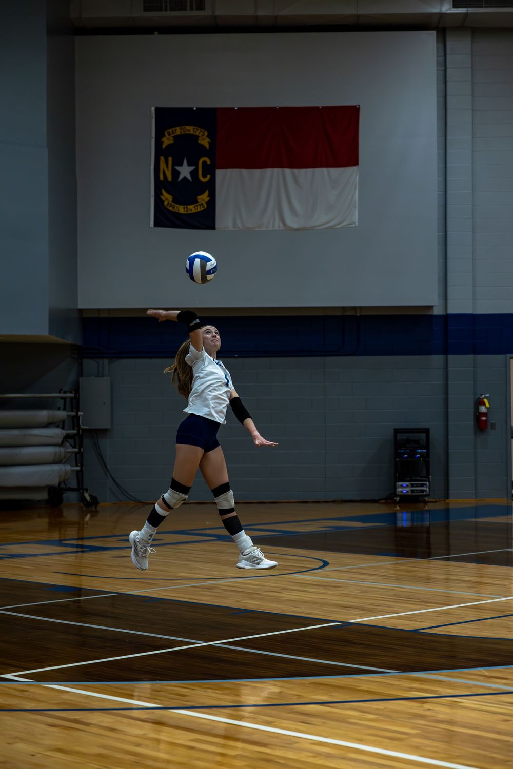 A volleyball player dives low to save a ball during an indoor match on a wooden court.