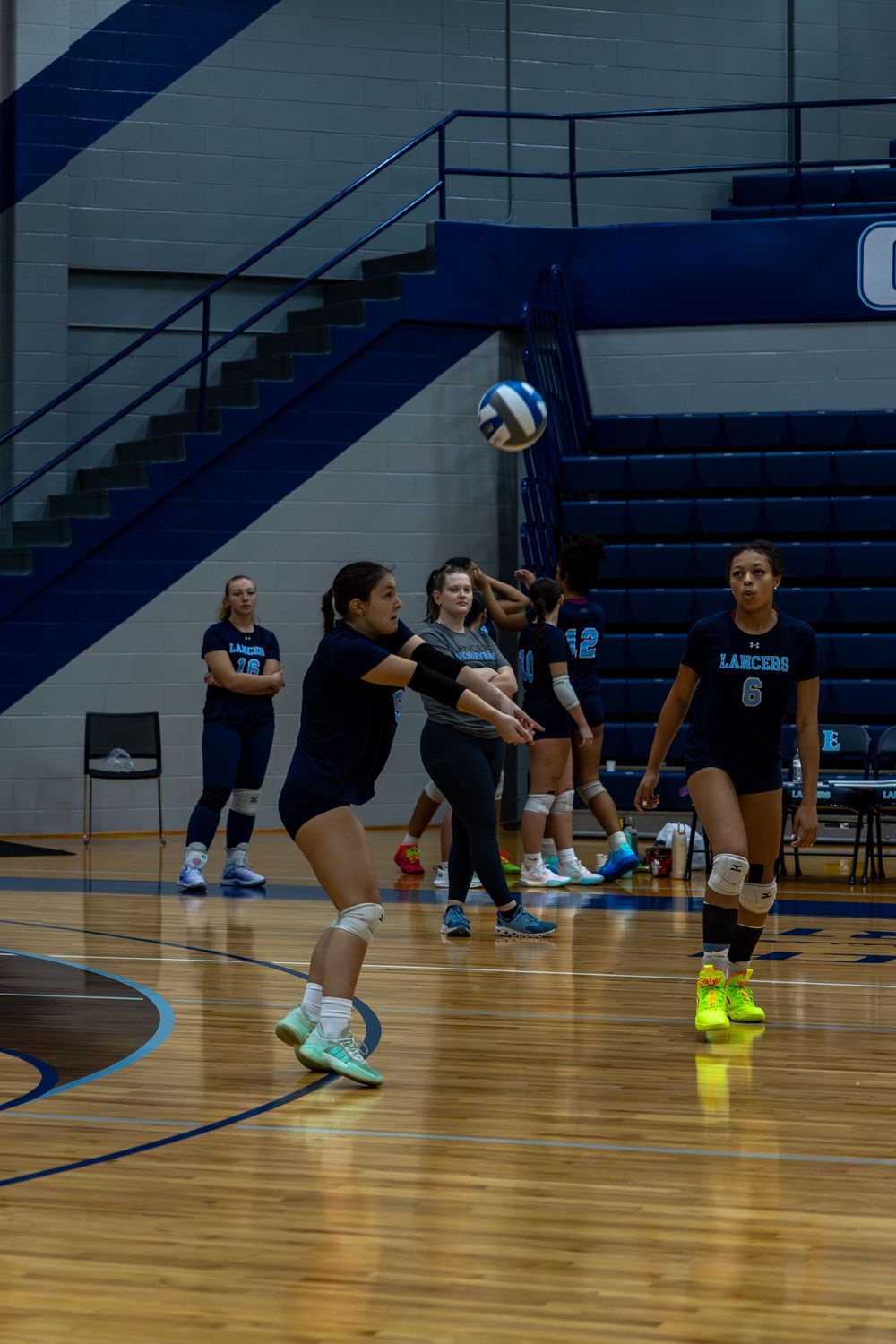 Indoor volleyball players practice diving drills on a wooden gymnasium floor during team training session.