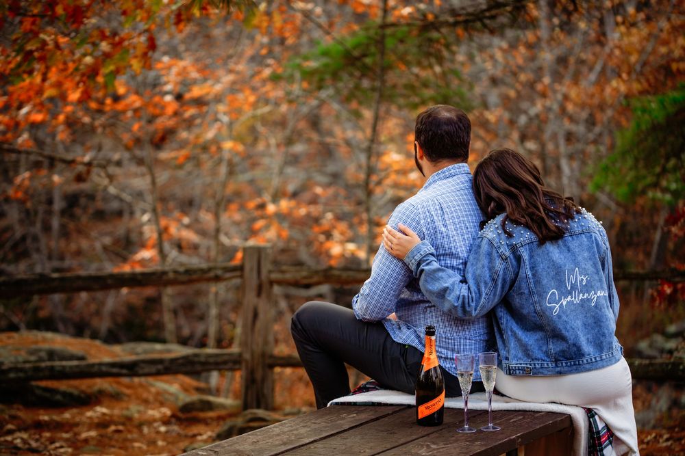 Couple sitting on wooden bench surrounded by vibrant autumn foliage in a peaceful park setting.