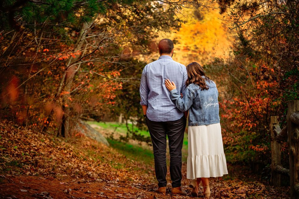 People walk along a winding autumn path surrounded by vibrant orange and red fall foliage in a park setting.