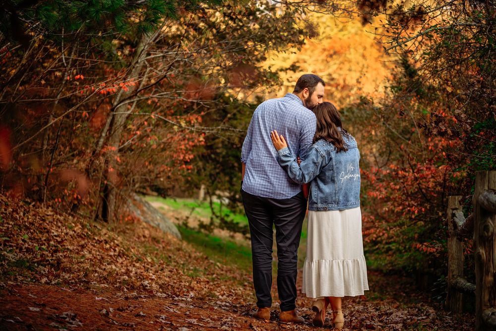 A couple shares an intimate moment while standing among autumn foliage during golden hour in a wooded area.