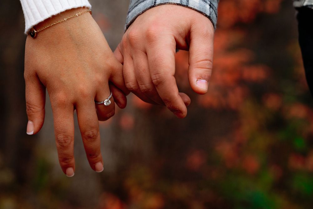 Close-up of hands holding and examining a small shiny ring with a gemstone in natural lighting.