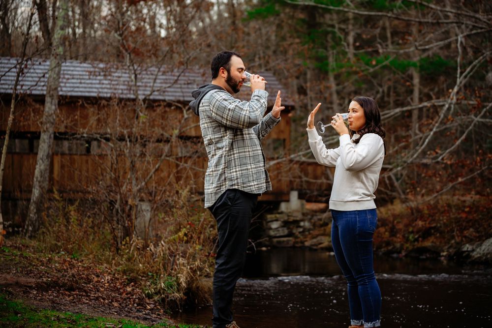 A couple stands on stone steps in a garden, playfully gesturing with their hands during a casual outdoor photoshoot.
