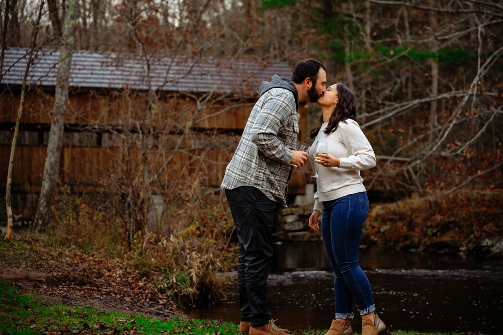 A couple embraces in a romantic outdoor photoshoot against a wooded autumn backdrop.