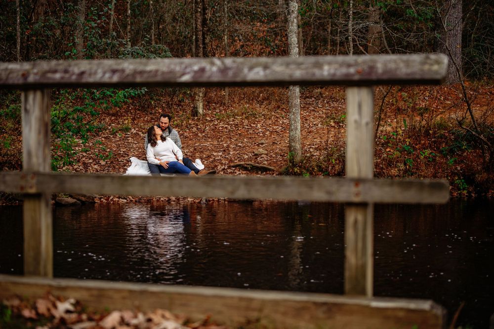 A couple sits together on a wooden dock overlooking a serene lake surrounded by autumn foliage.