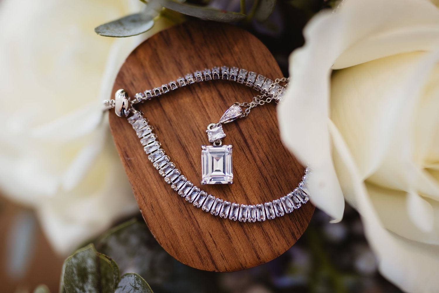 Elegant diamond necklace and jewelry pieces displayed on wooden surfaces with white rose petals.
