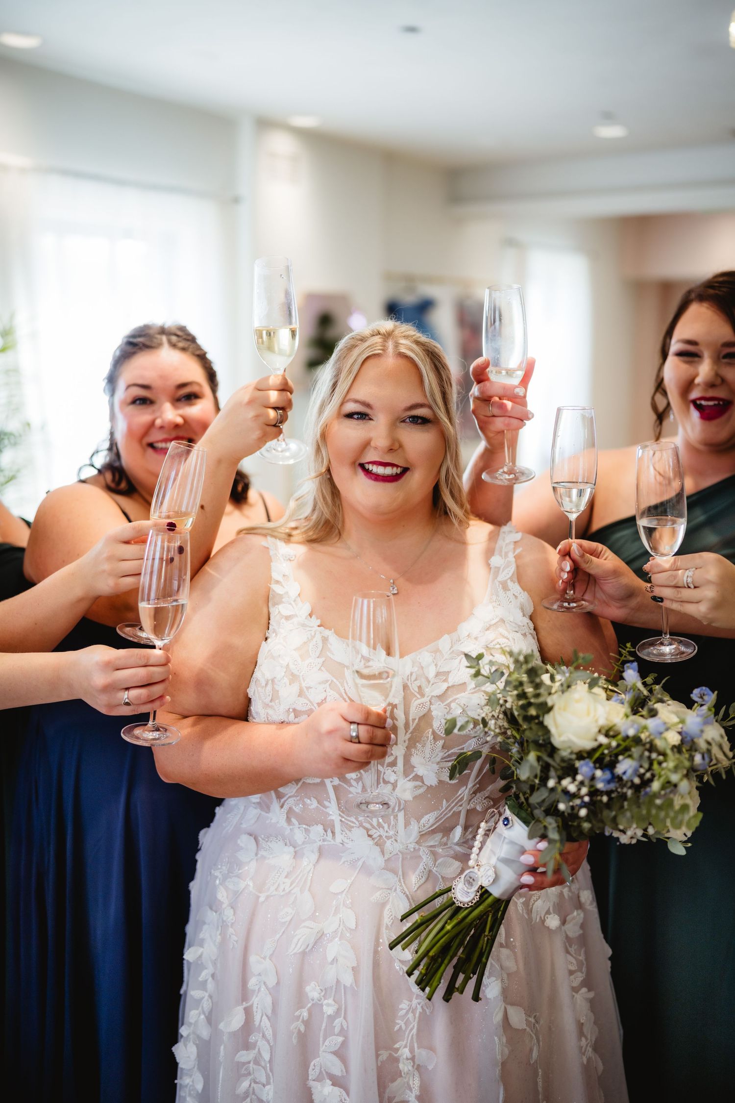A group of wedding attendees in navy and white dresses raise champagne glasses in celebration during a joyful toast.