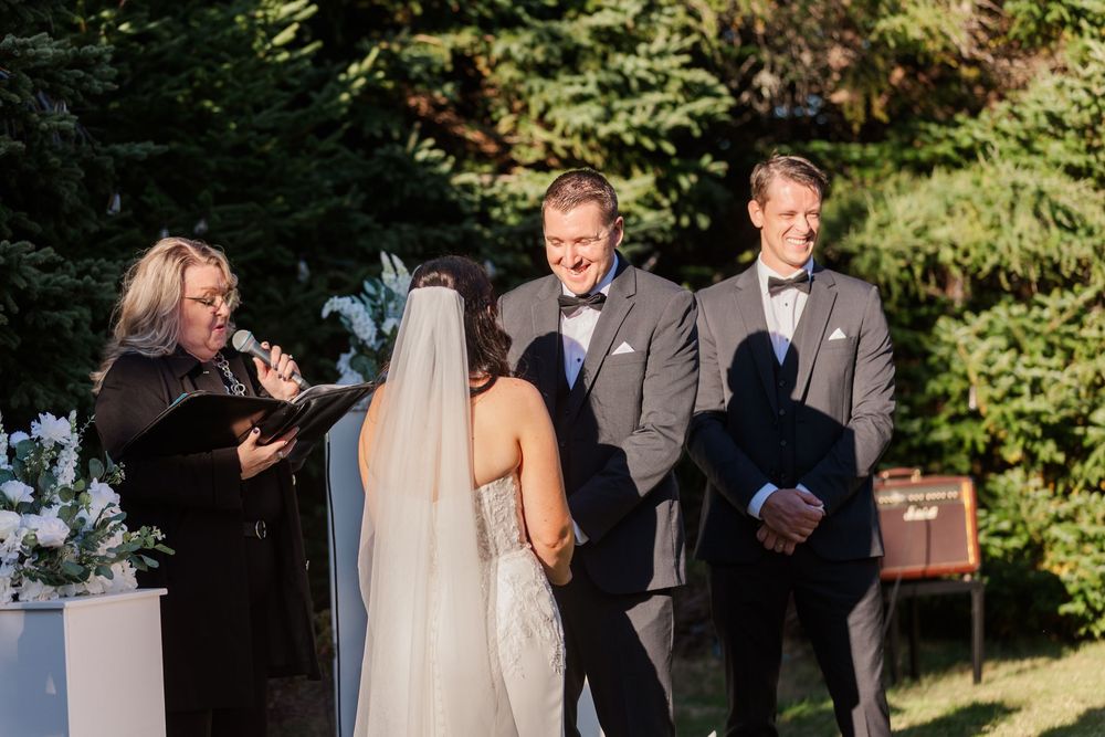 Outdoor wedding ceremony in a lush garden setting with guests in formal attire.