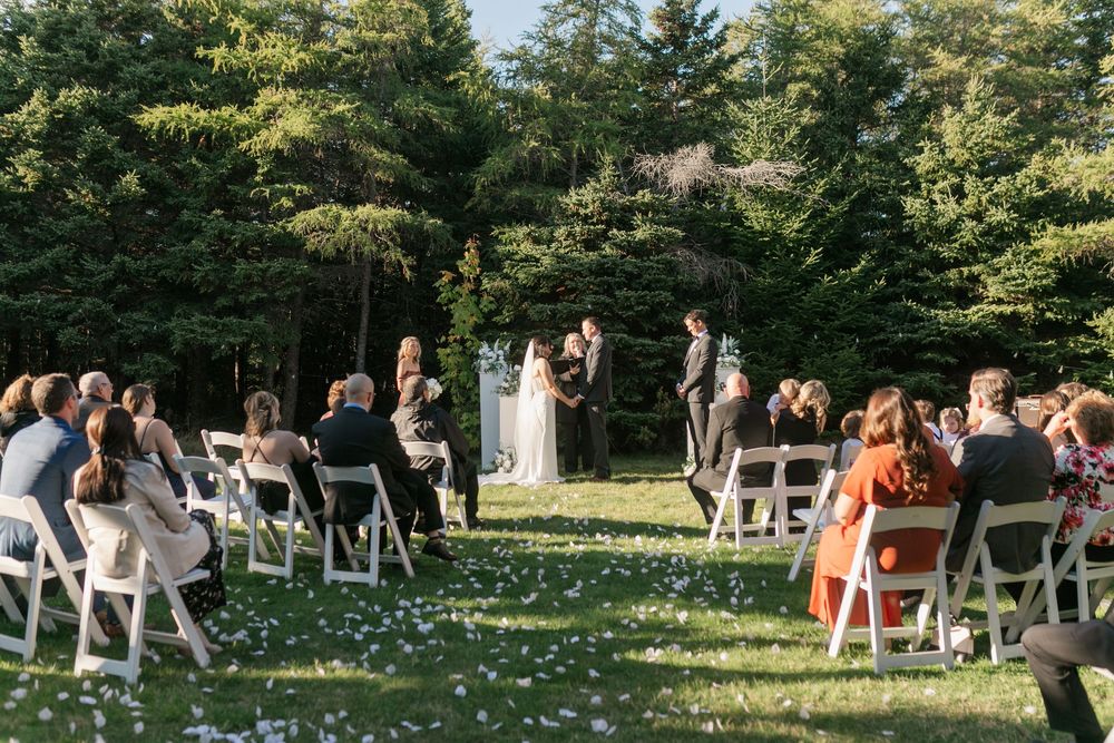 Wedding ceremony setup in a lush garden with white chairs arranged in rows and orange floral decorations.