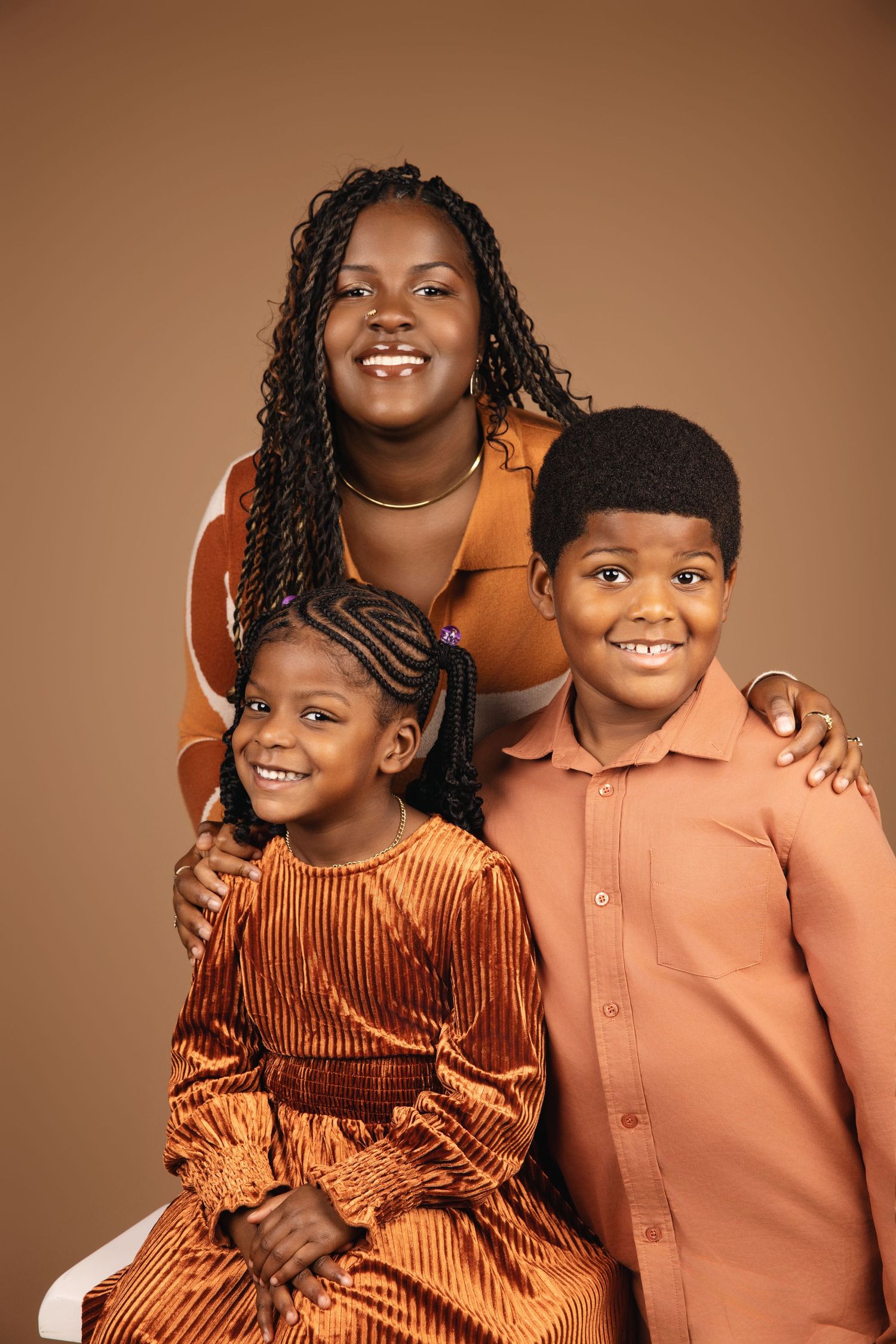 Two siblings share joyful laughter while posing together against a brown backdrop wearing orange and peach tones.