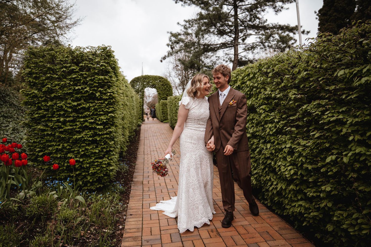 Bridesmaids in yellow dresses react with joy and surprise as bride reveals her wedding dress outdoors.