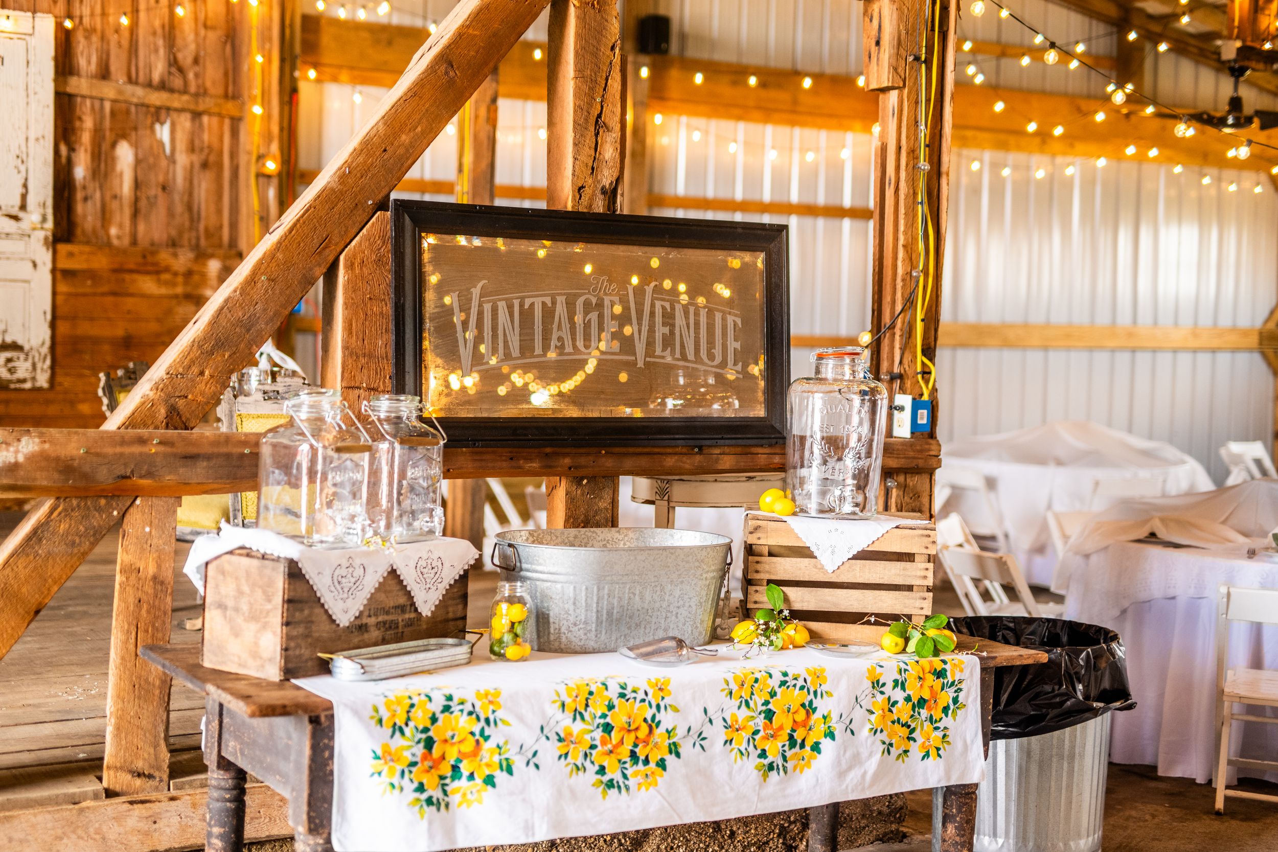 Rustic barn wedding reception setup with vintage decor, wooden crates, and yellow sunflower arrangements on white tablecloths.