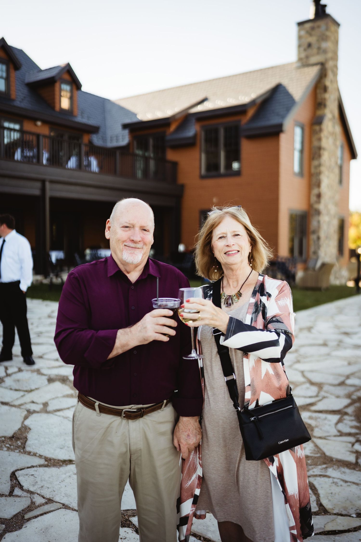 Wedding guests enjoying drinks and conversation on a stone patio outside a rustic venue.