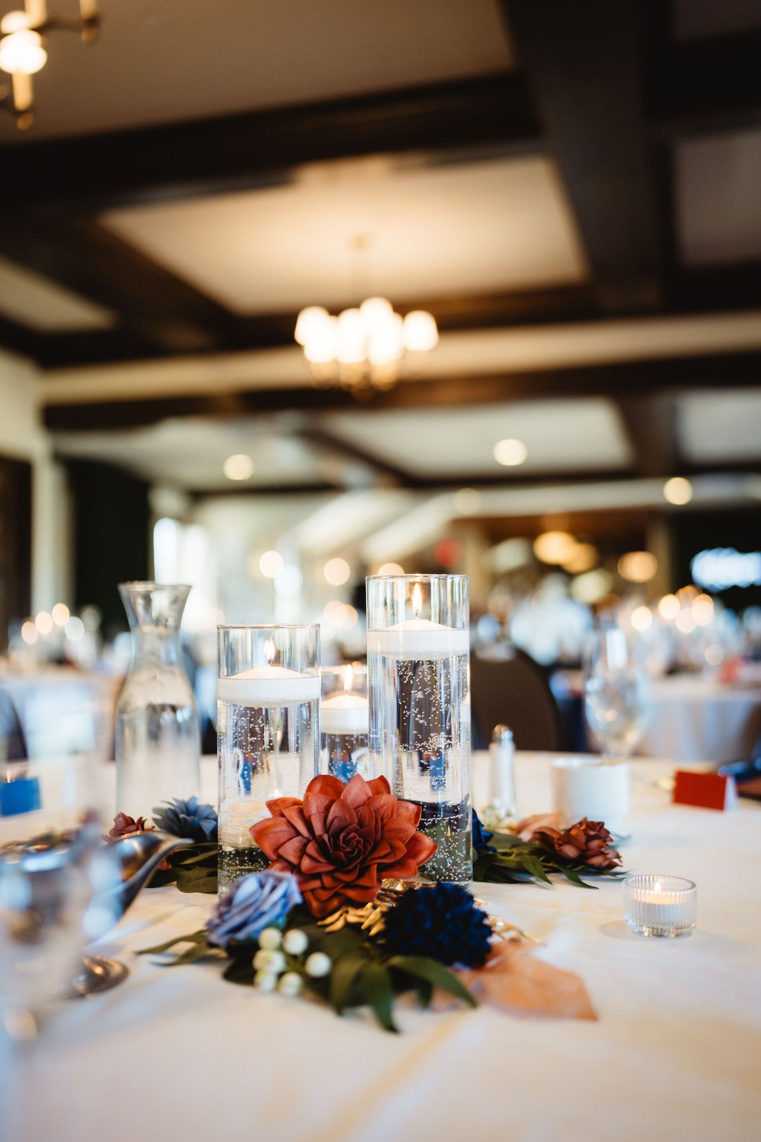 Reception table settings with white linens and floral centerpieces featuring red and blue blooms.