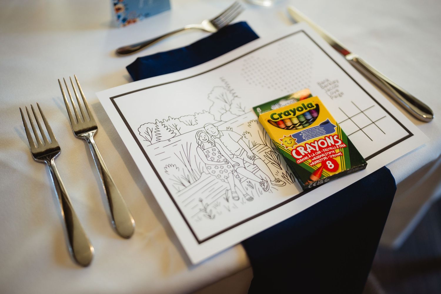 Place settings at a restaurant table with silverware, paper placemats and a box of crayons.
