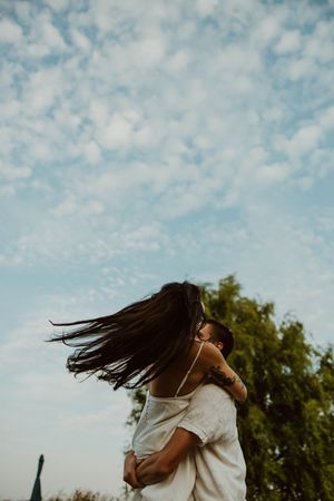 A couple spins and dances together under a cloudy blue sky.