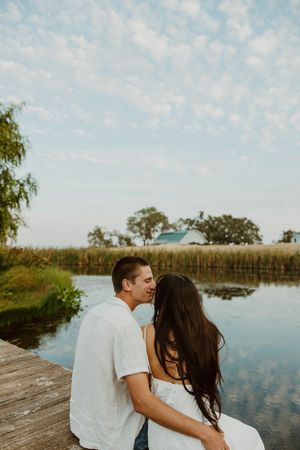 A couple shares an intimate moment on a lakeside dock during golden hour.