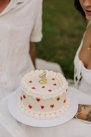 A white frosted cake decorated with small red hearts and a gold number one topper.