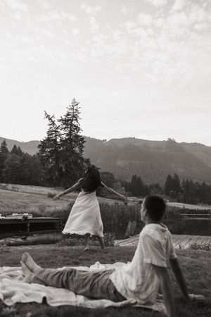 Black and white photo of couple relaxing on blanket with mountain landscape behind them.