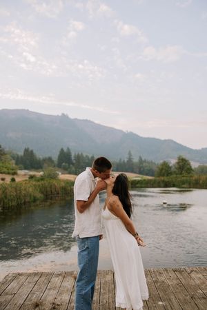Romantic couple shares intimate moment on wooden dock by mountain lake.