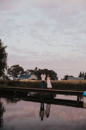 Silhouettes of people standing on a dock at dusk with pink sky reflections in the calm water.