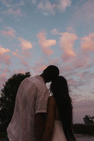 A romantic couple embraces against a pink and blue sunset sky with clouds.