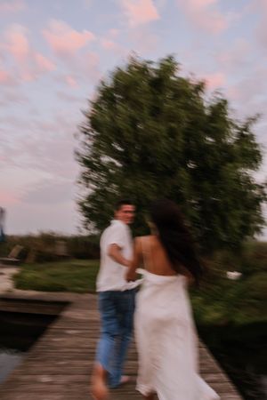 A couple in casual attire shares an intimate moment on a wooden boardwalk at sunset.