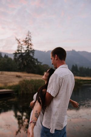 Two people share a tender moment on a dock overlooking a mountain lake at dusk.