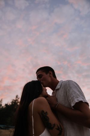 A romantic silhouette of a couple kissing against a pink cloudy sky at dusk.