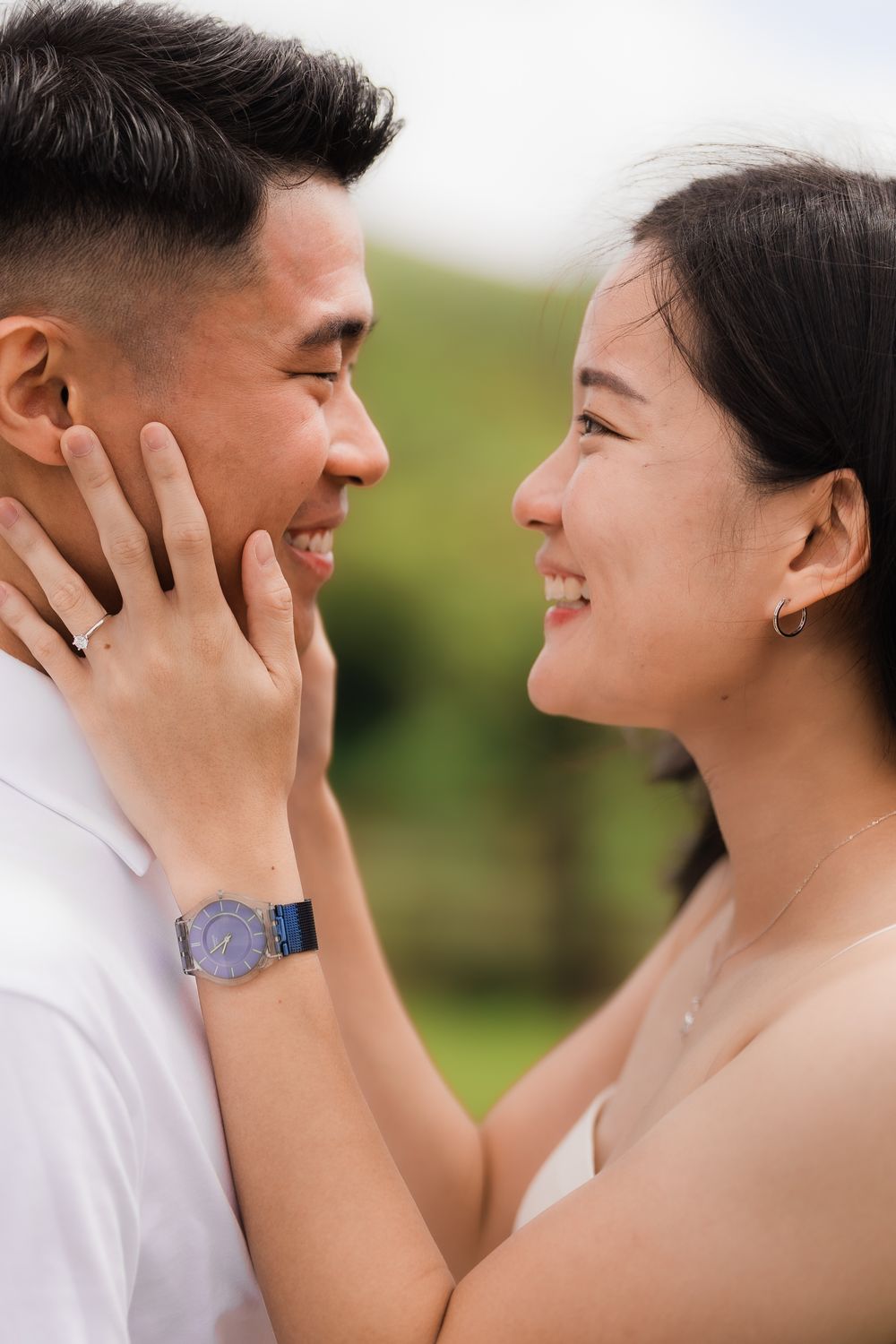 Close-up shot of a couple with the woman wearing an engagement ring joyfully holding the man's face